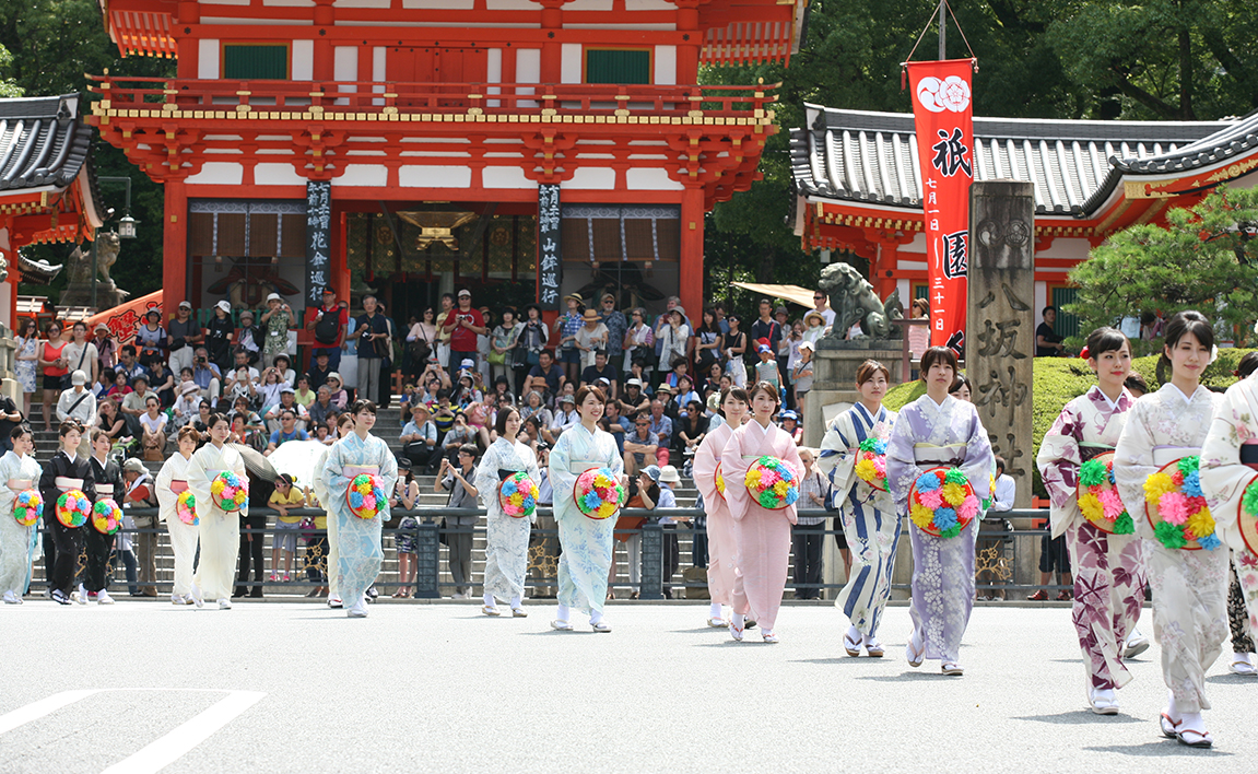 花を付けた傘を持ち和服で四条を歩く参加者